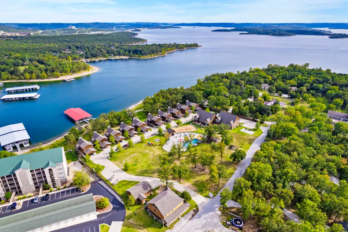 A panoramic exterior view that captures the lake, residential buildings, a swimming pool, and abundant surrounding greenery. The setting is lively yet relaxing, with opportunities for boating, swimming, hiking, and family gatherings.
