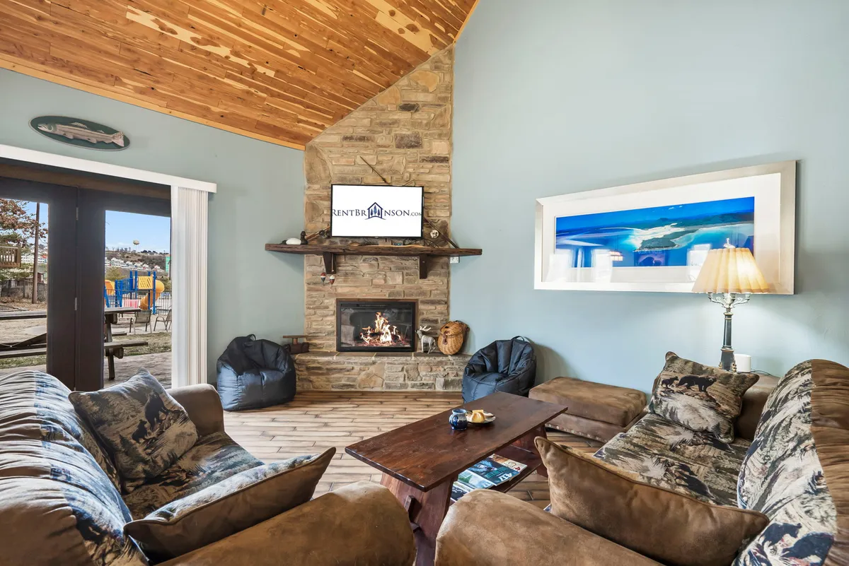 A cozy, comfortable interior living room featuring a stone fireplace, plush sofa seating, a TV, and tasteful artwork. The setting is ideal for relaxing evenings after a day of outdoor fun and ensures a clean, inviting space for all guests.