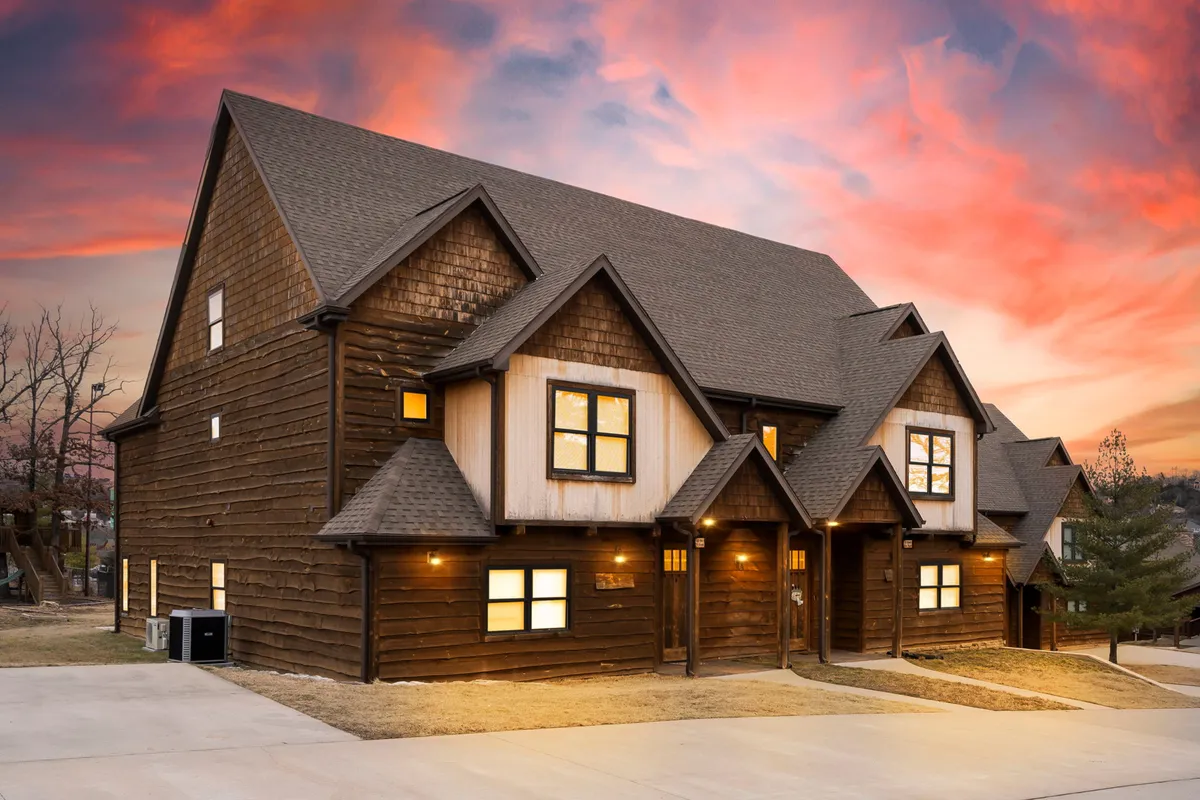 A welcoming exterior view of the property, showcasing the wooden facade, large windows, and a cozy porch. The setting evokes evenings spent watching sunsets and enjoying barbecues with family and friends after a day exploring local attractions.