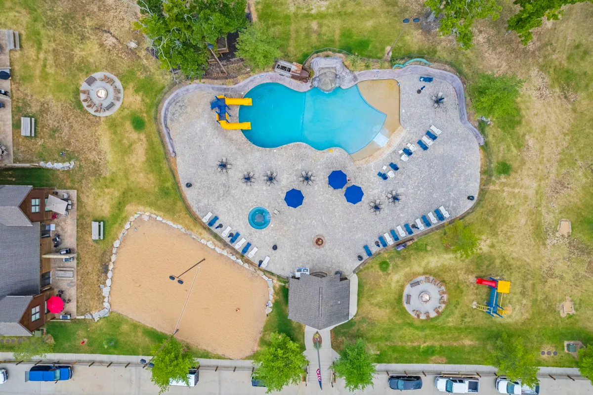 A vibrant exterior scene showcasing a swimming pool, sand volleyball court, playground area, and ample lounge chairs. Families are swimming, sunbathing, playing volleyball, and kids are having fun on playground equipment, all set within a cheerful and communal resort atmosphere.